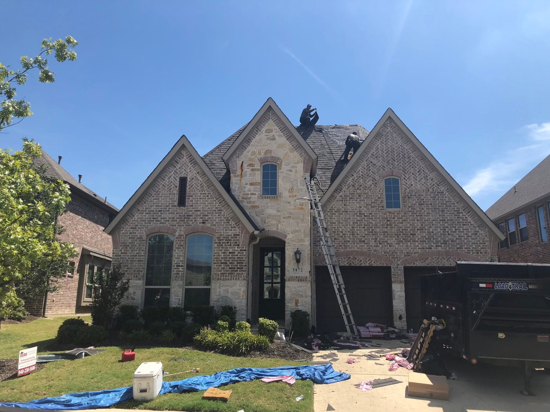 Brick house exterior with ladders, roof work, and construction materials in the front yard