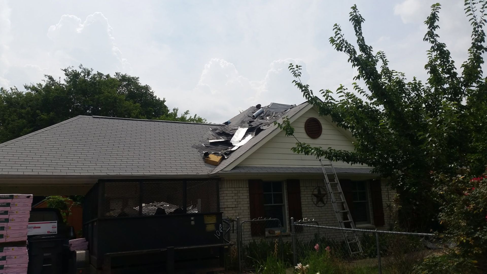 Damaged house roof with debris and a large hole near the ridge after storm damage