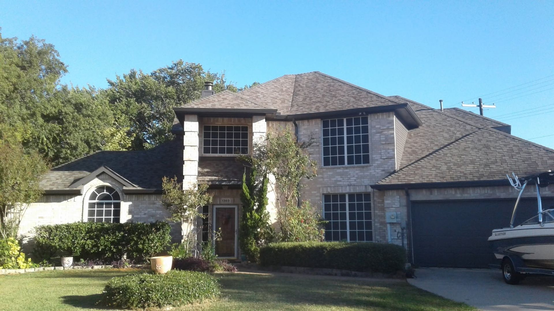 Suburban two-story brick house with dark roof, attached garage, and well-kept front yard in bright sunlight