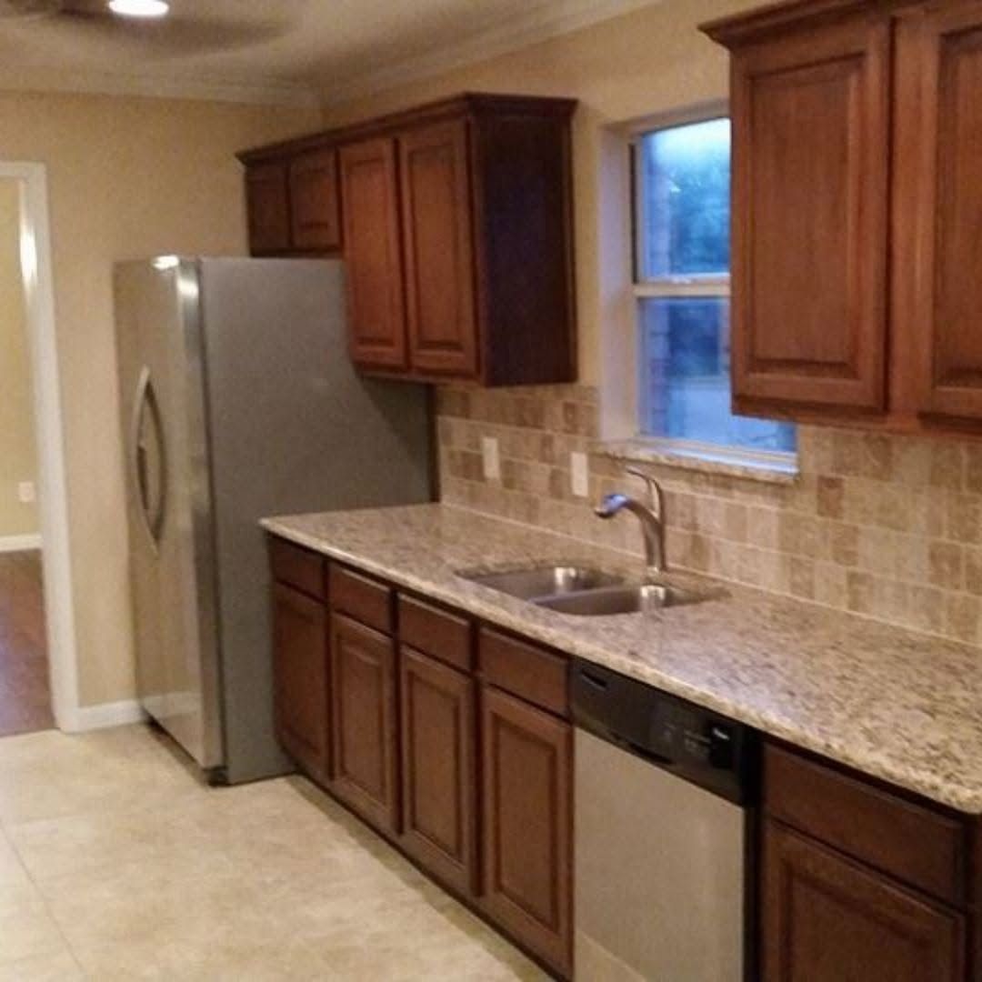 Empty modern kitchen with wood cabinets, granite counters, stainless fridge, and tiled backsplash