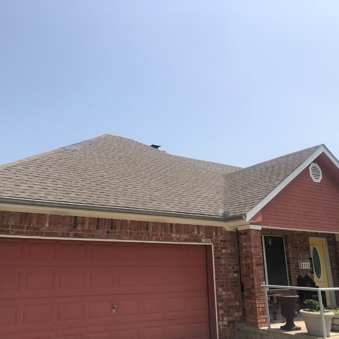 Brick house with red garage doors and a shingled roof under a clear blue sky