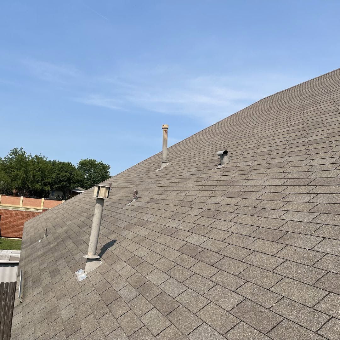 Close-up of a sloped gray shingle roof with vents and a blue sky above