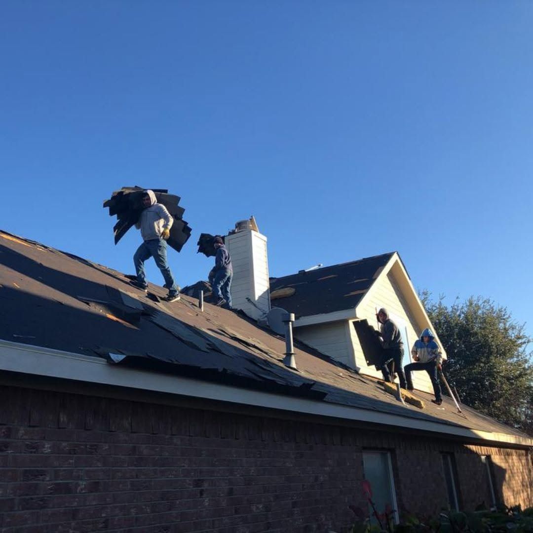 Roofers working on a house roof under a clear blue sky.