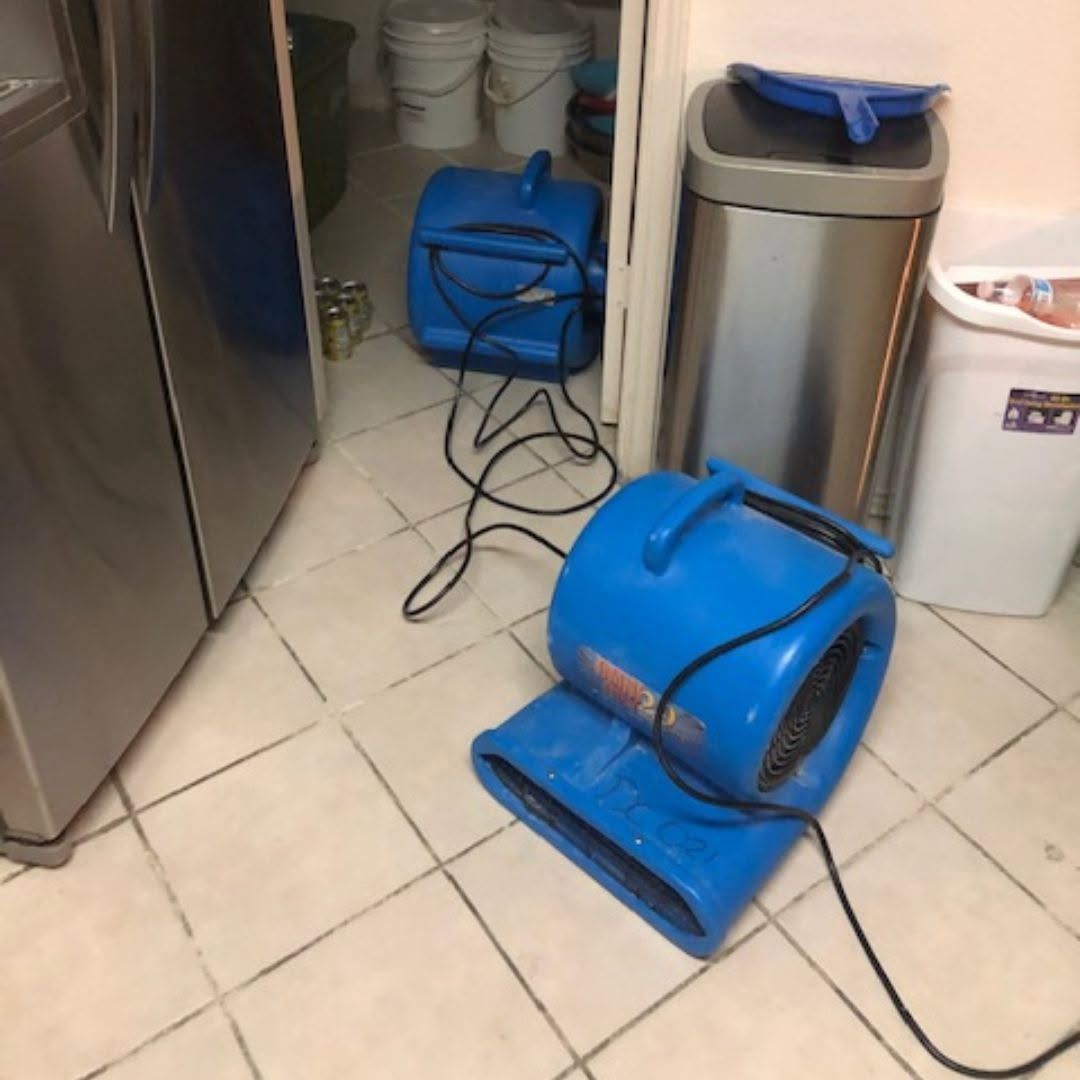 Two blue floor dryers on tiled floor in a utility room, with cords and trash bins nearby