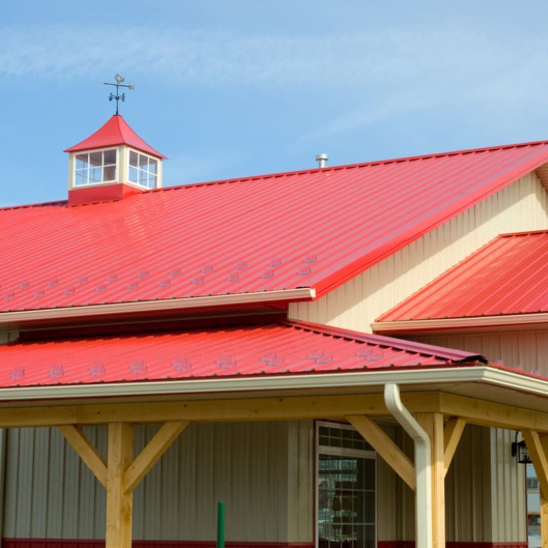 Red-roofed barn or farm building with beige siding and a small cupola under a blue sky