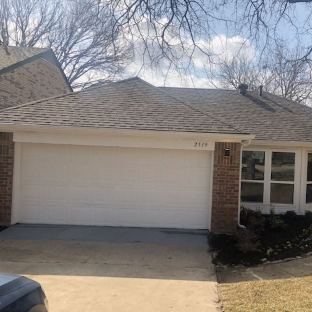 Suburban house with white garage door, brick facade, and front windows under a cloudy sky