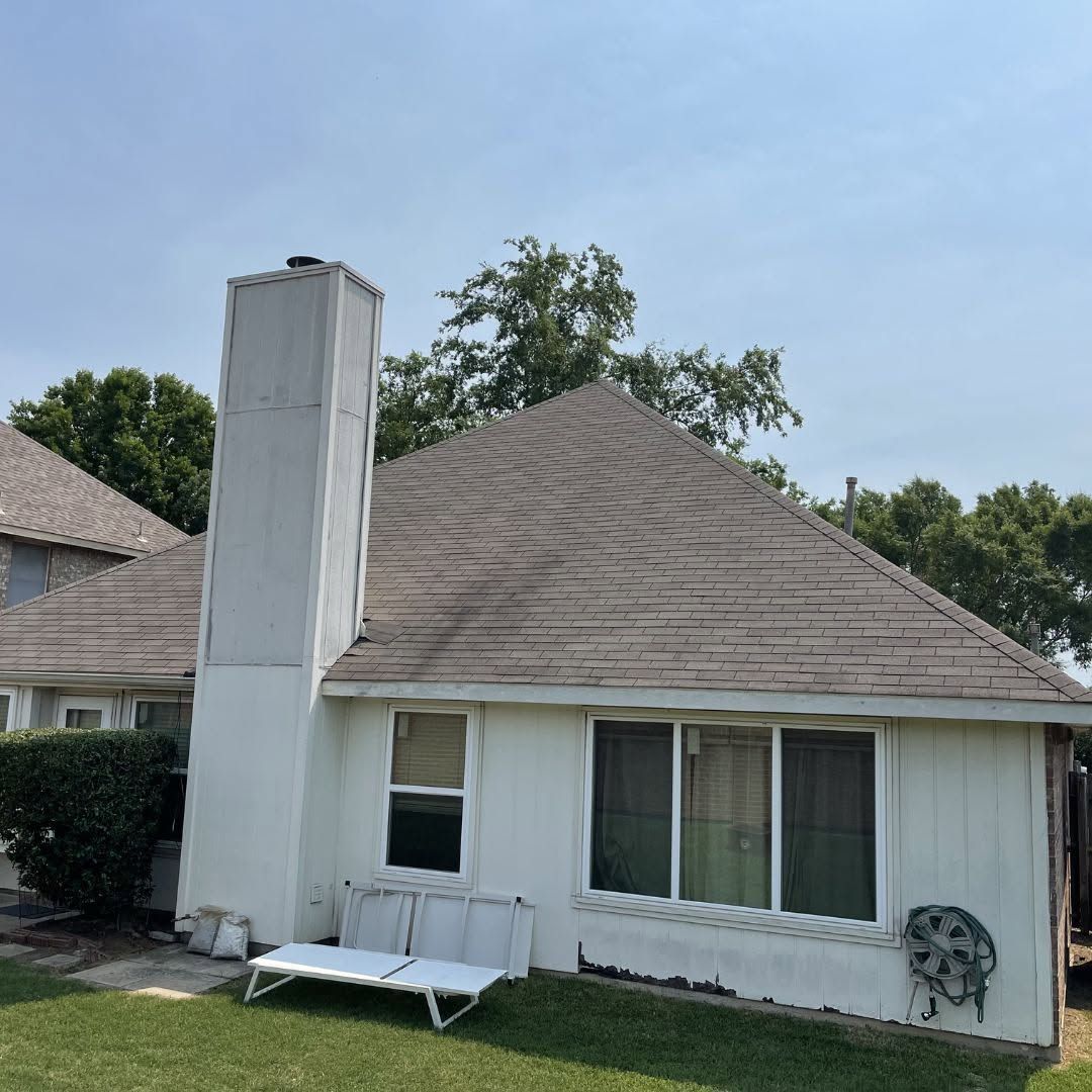 White house exterior with a tall chimney, tan shingled roof, and a small front bench under windows