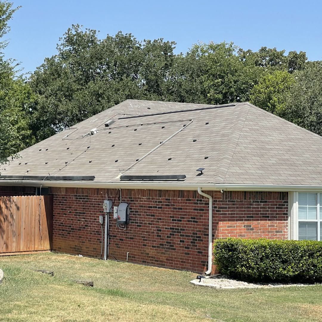 Single-story brick house with gray roof, wooden fence, and trimmed bushes under a blue sky