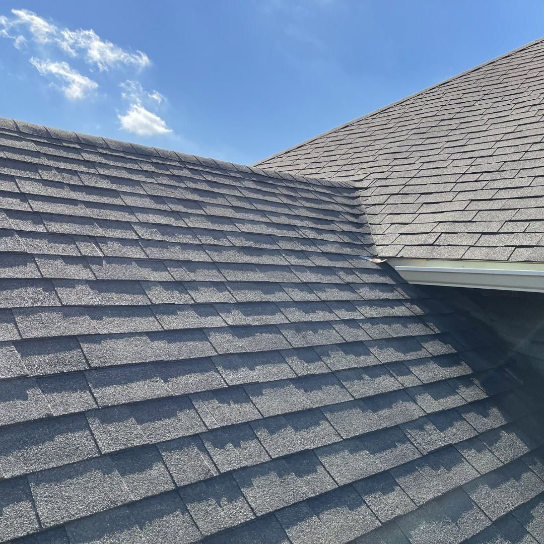Gray shingled roof under a blue sky with clouds, showing a roof valley and dormer edge
