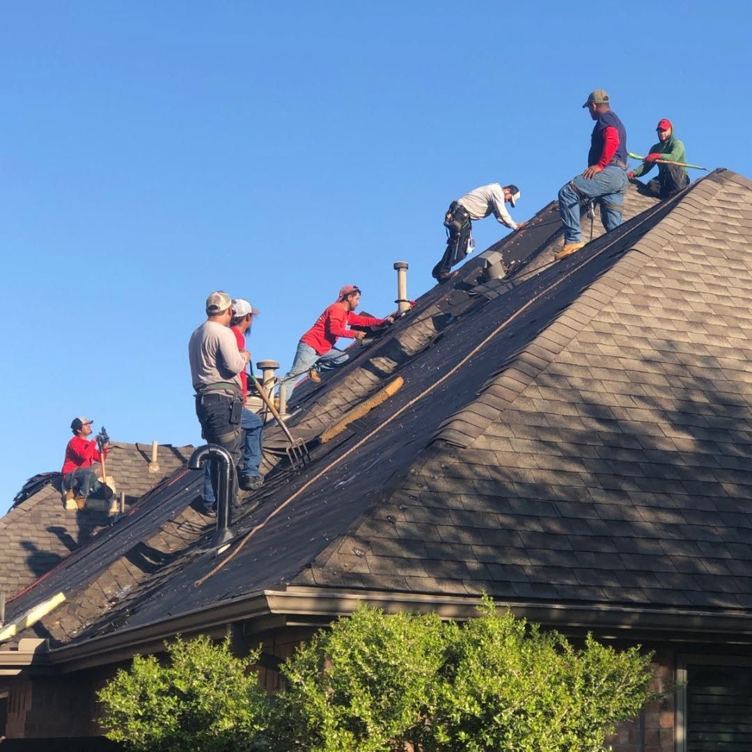 Workers roofing a steep house roof, installing shingles under a clear blue sky
