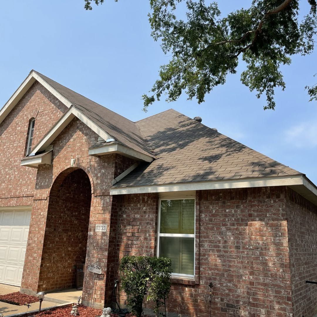 Brick suburban house with arched front entry, tan shingled roof, and a tree branch overhead