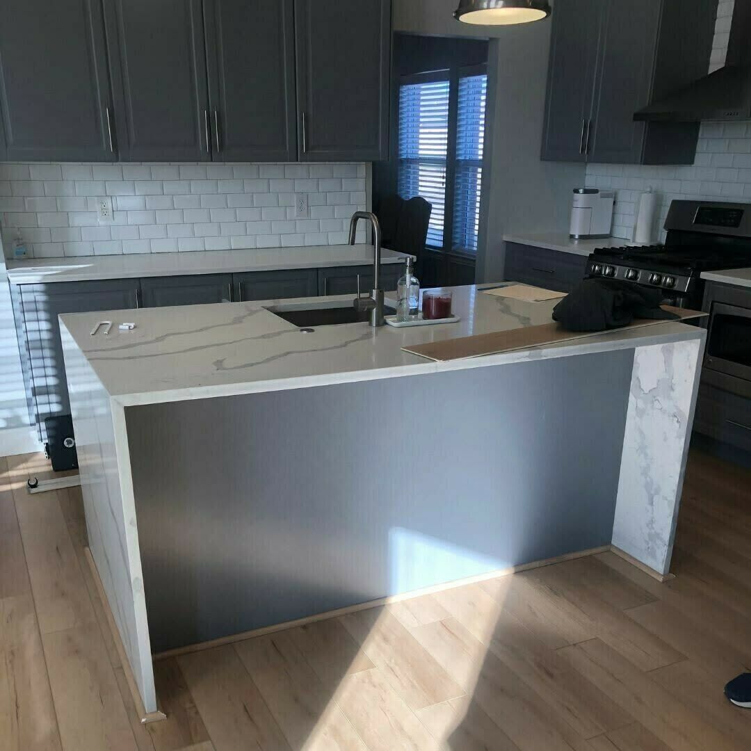 Modern kitchen with a white island, dark cabinets, stainless range, and wood floor.