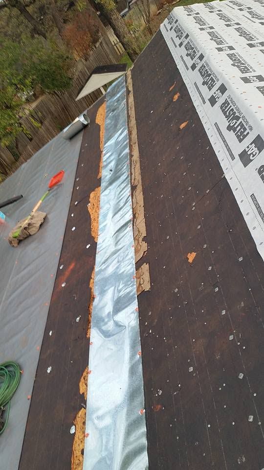 Roof under repair with blue underlayment, white membrane, and scattered tools on dark shingles