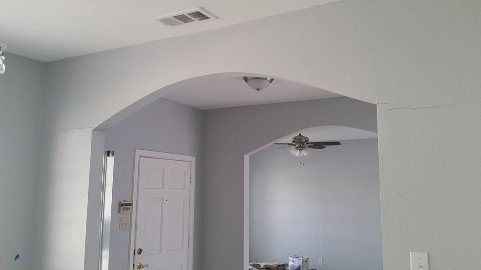 Empty gray interior room with arched doorway, white door, and ceiling fan in the adjacent room
