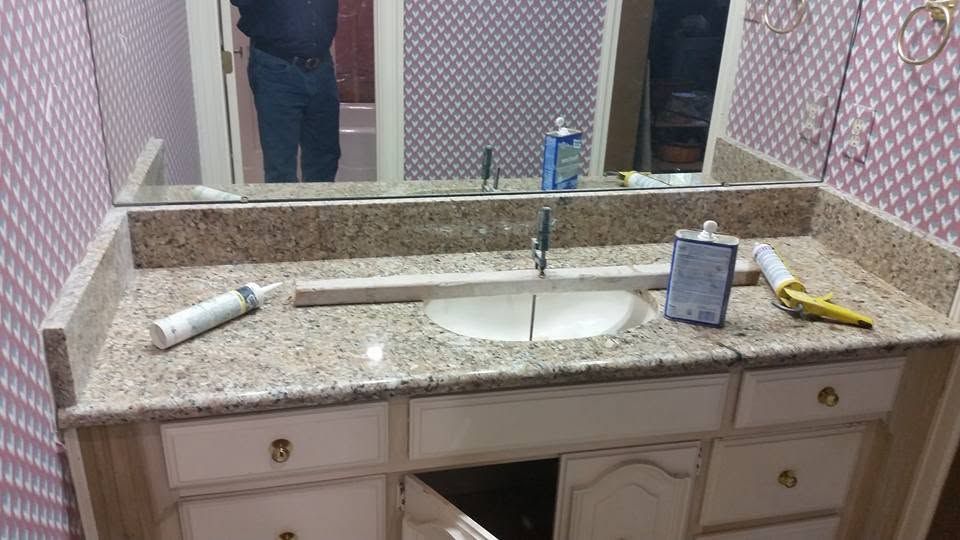 Bathroom vanity with granite counter, sink, mirror, and cleaning items scattered on top