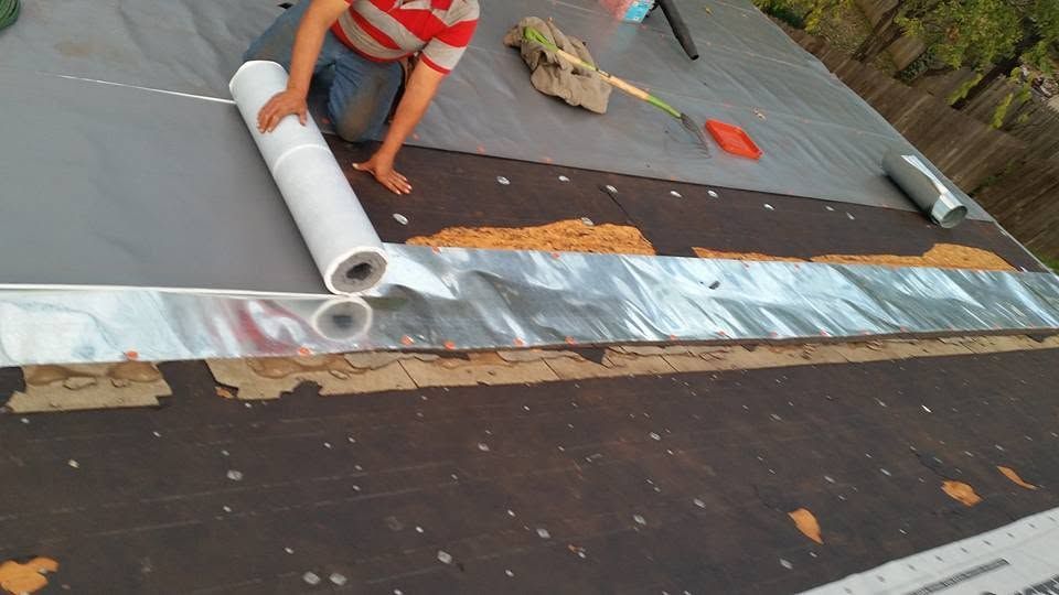 Worker rolling white roofing membrane over a partially installed roof with dark underlayment.