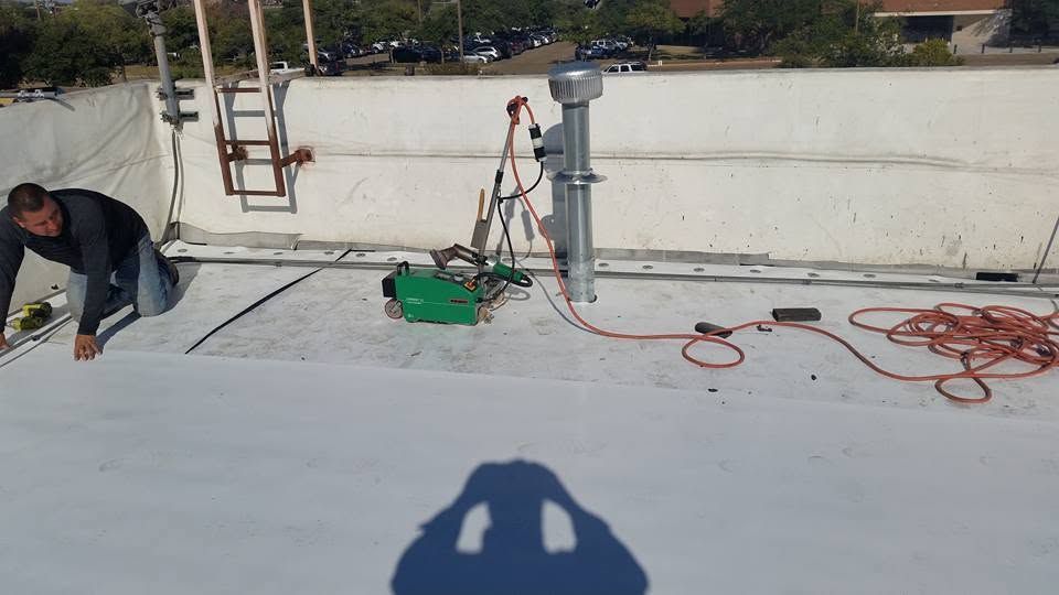 Worker on a white rooftop near a ladder, tools, and coiled hose.