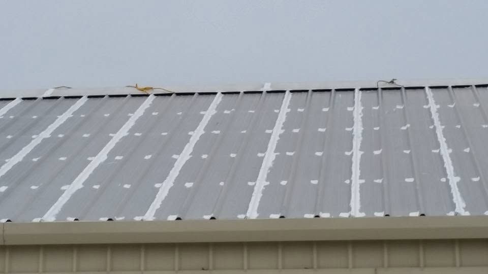 Close-up of a gray metal roof with snow patches and a tan building edge below