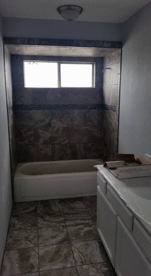 Small bathroom with a tub, window, tiled floor, and white vanity with drawers.