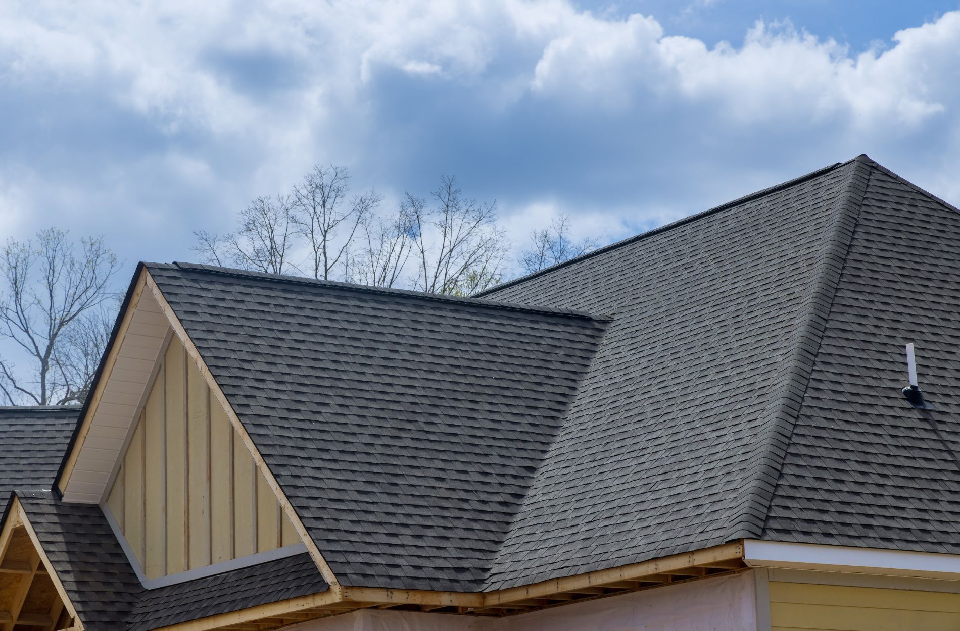 Suburban house roof with gray shingles against a cloudy sky