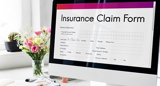 Insurance claim form displayed on a desktop monitor beside a desk with flowers and notes