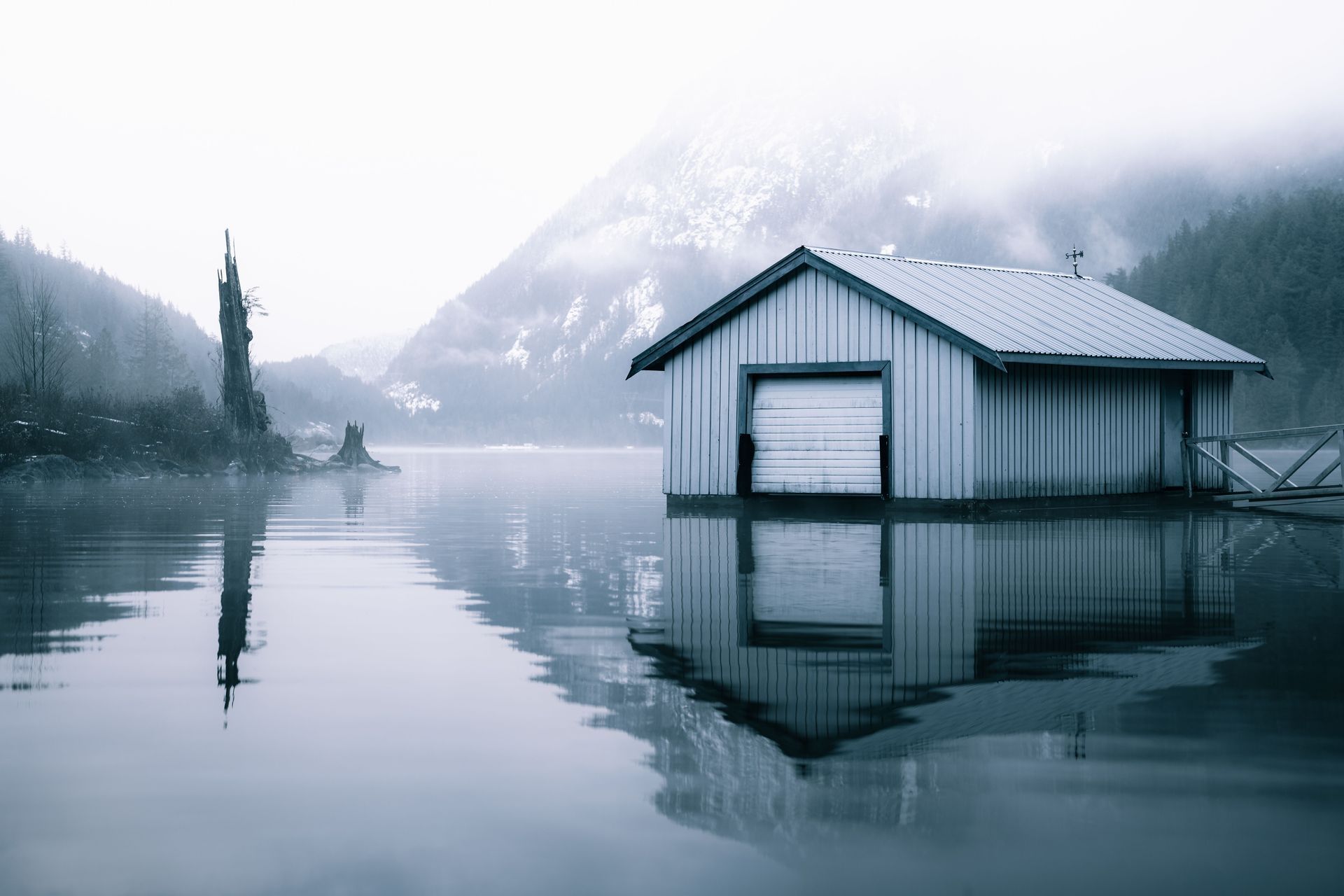 Snowy mountain lake with a small boathouse reflected in calm water at dawn