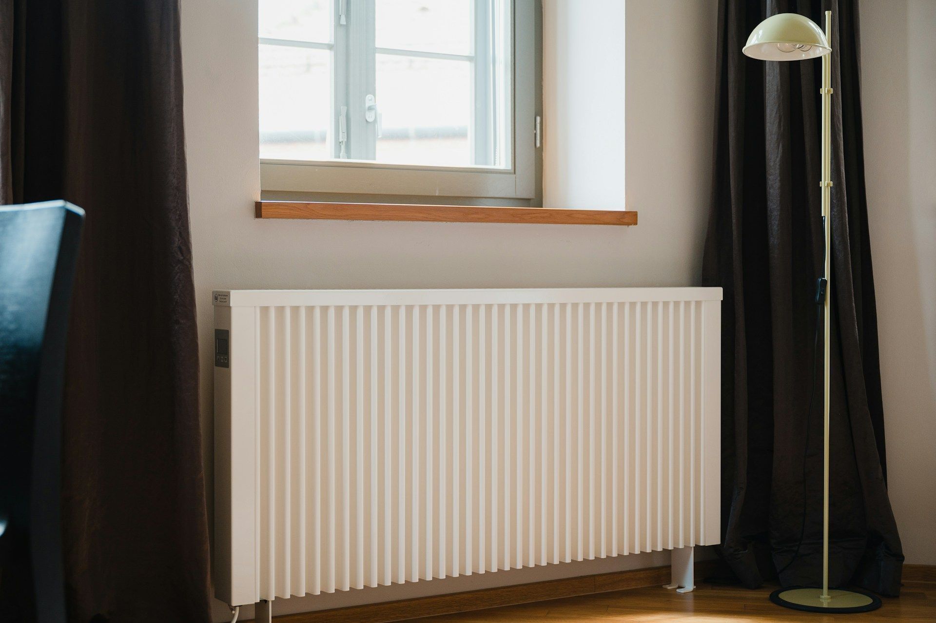 Minimal room with a window, radiator, and floor lamp beside dark curtains.