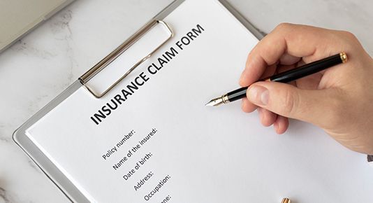 Hand writing on an insurance claim form with a black pen on a clipboard