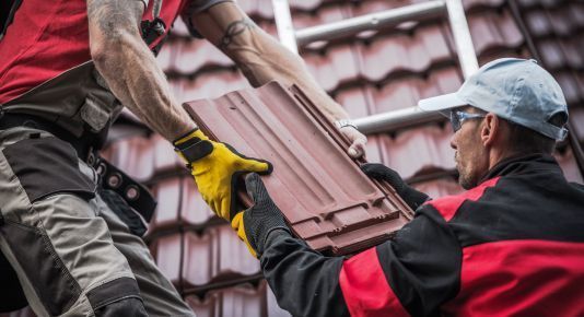 Two workers passing roof tiles on a red-tiled roof