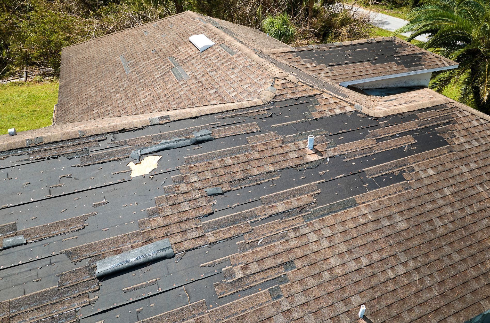 Damaged shingle roof with missing sections and exposed underlayment on a house