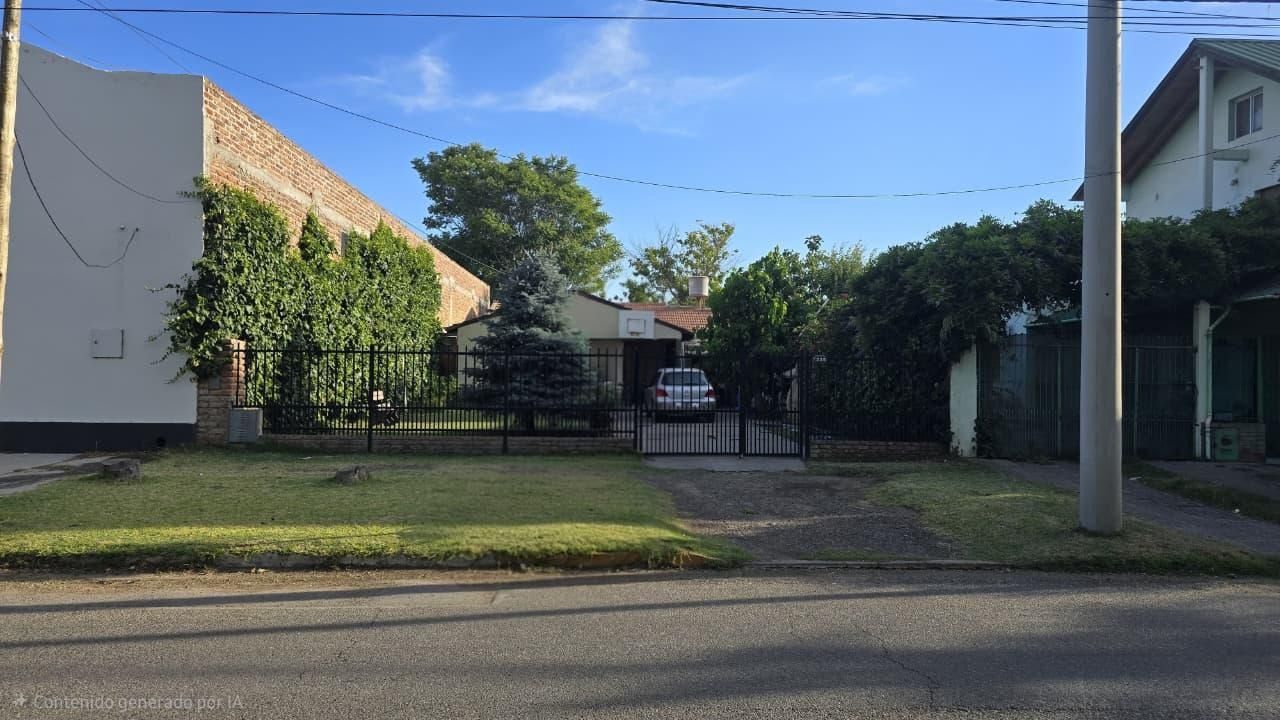 Entrada a una casa residencial con camino de acceso cerrado, césped verde, árboles y una calle tranquila al frente.
