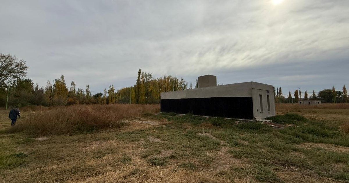 Campo de hierba bajo un cielo nublado, con árboles a lo lejos y una estructura de hormigón a la derecha.