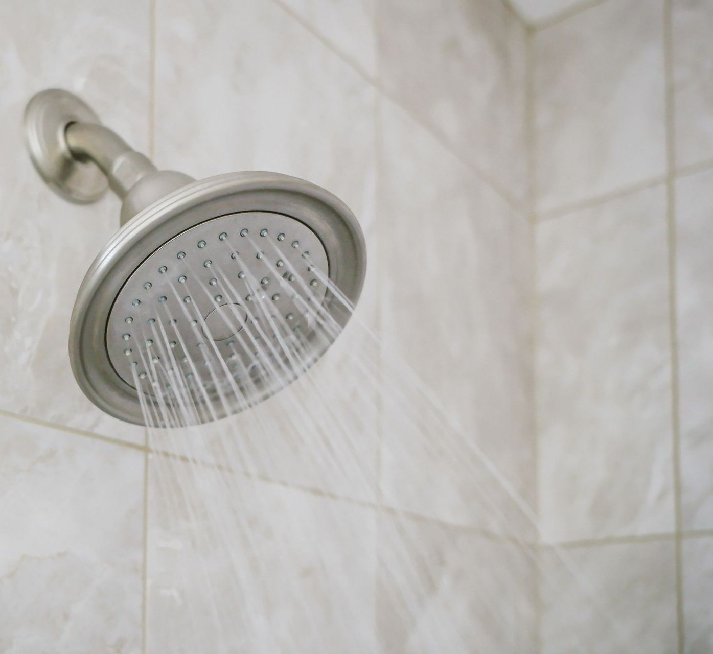 Showerhead spraying water against tiled wall.