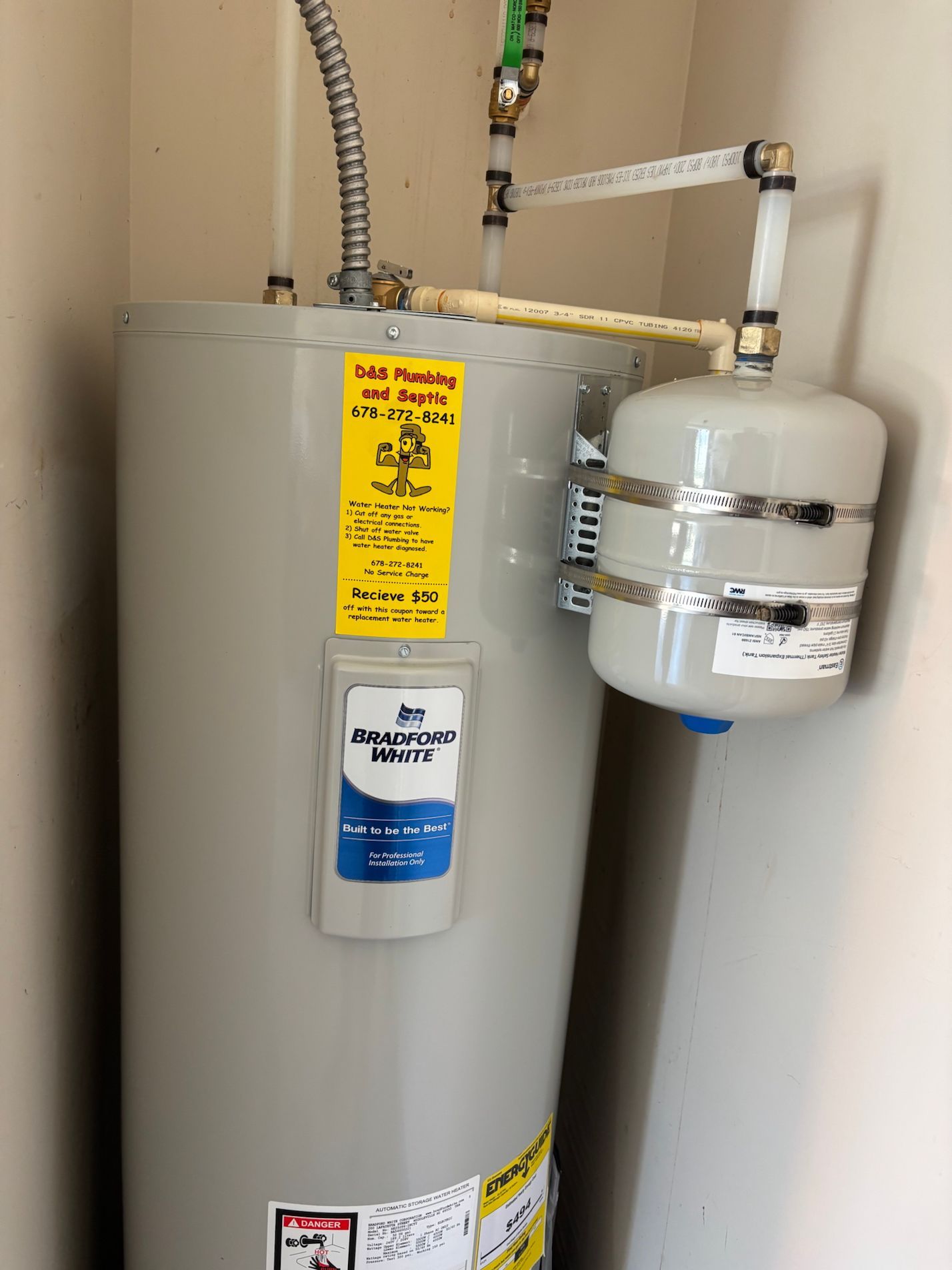 A hot water heater with an expansion tank in a small, beige-walled space.