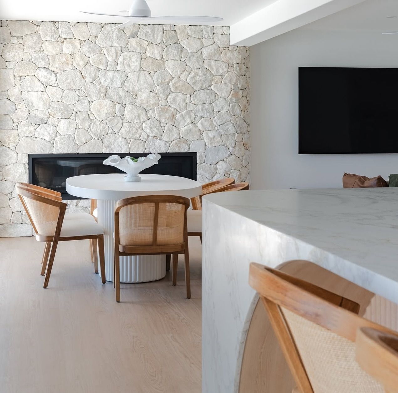 Dining area with stone wall, round table, chairs, and a large black television — Totally Flooring Gold Coast In Bundall, QLD