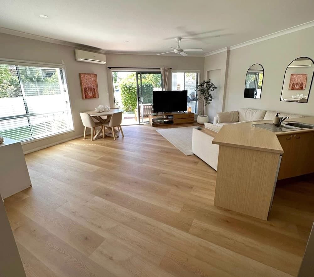 A Living Room With Hardwood Floors, a Couch, a Television, a Table and Chairs — Totally Flooring Gold Coast In Bundall, QLD