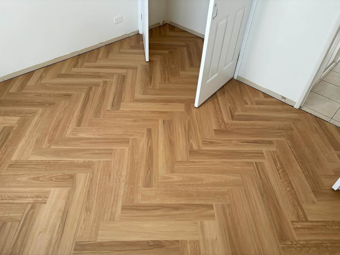 A Wooden Floor With a Herringbone Pattern in a Room With a Door Open — Totally Flooring Gold Coast In Bundall, QLD