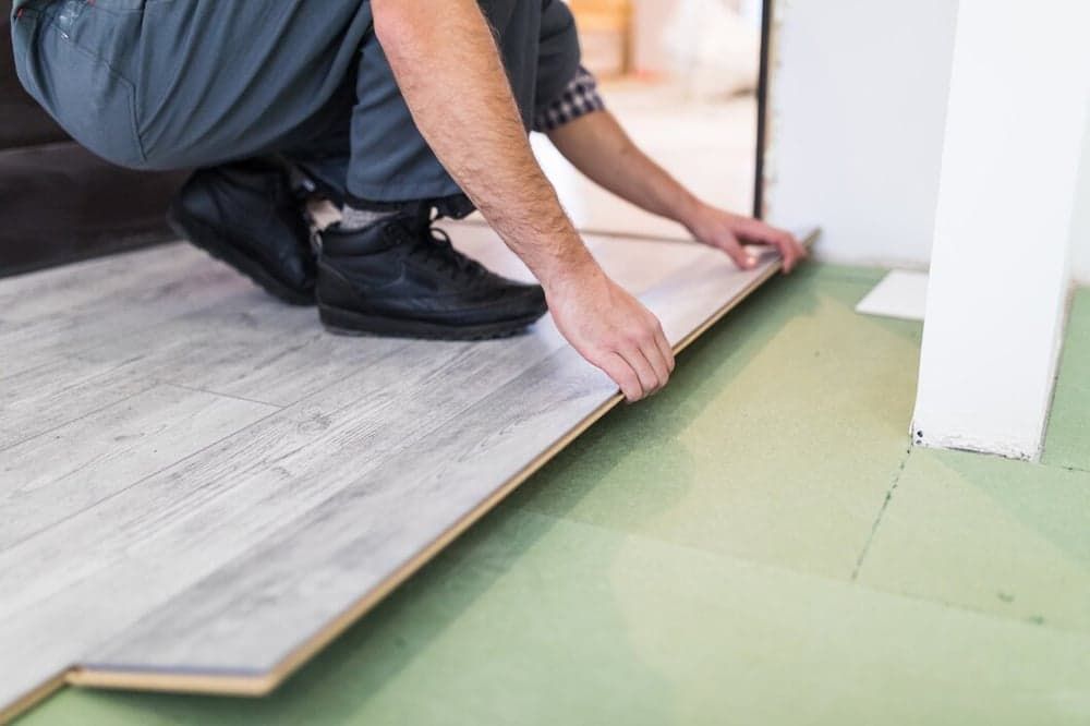 A Man is Installing a Wooden Floor in a Room — Totally Flooring Gold Coast In Bundall, QLD