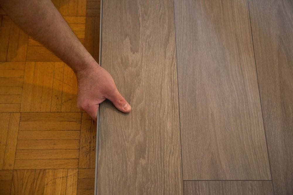 A Person is Holding a Piece of Wood on a Wooden Floor — Totally Flooring Gold Coast In Bundall, QLD