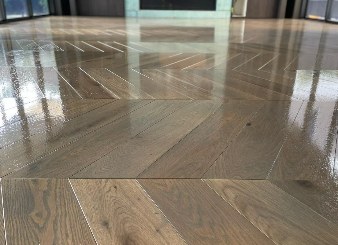 A close up of a wooden floor in a living room with a fireplace in the background.
