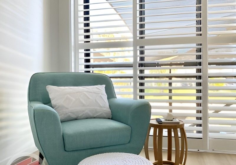 Light Blue Armchair with Pillow Beside a Small Wooden Side Table in A Bright Room with Window Blinds — Totally Flooring Gold Coast In Bundall, QLD