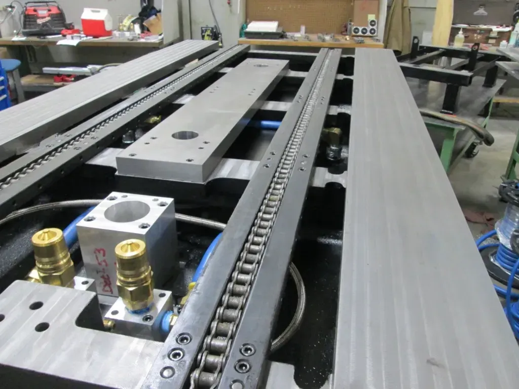 Industrial machine rails and chain drive assembly in a workshop, shown close-up on a metal frame.