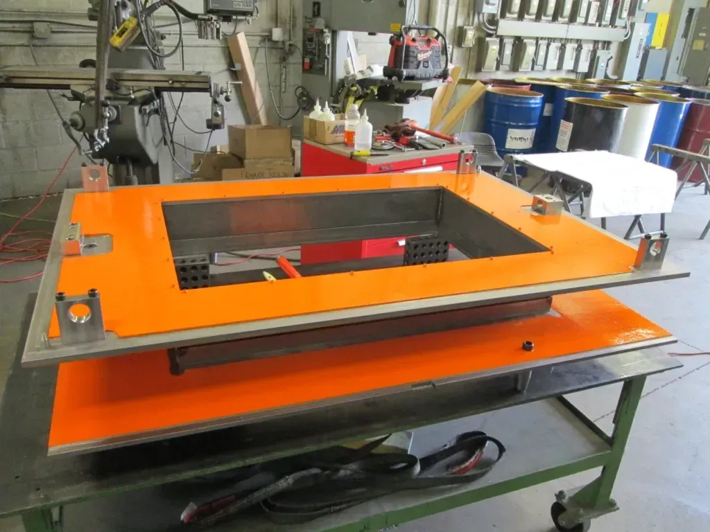 Orange industrial machine on a workbench in a workshop, with a black cable and metal frame.