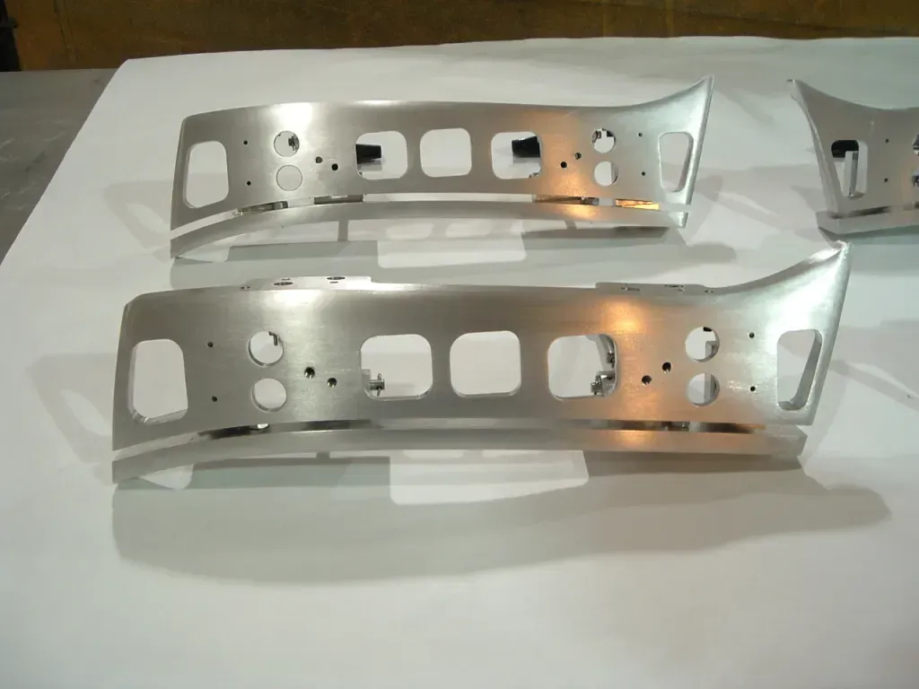 Two shiny perforated metal brackets lying on a white surface