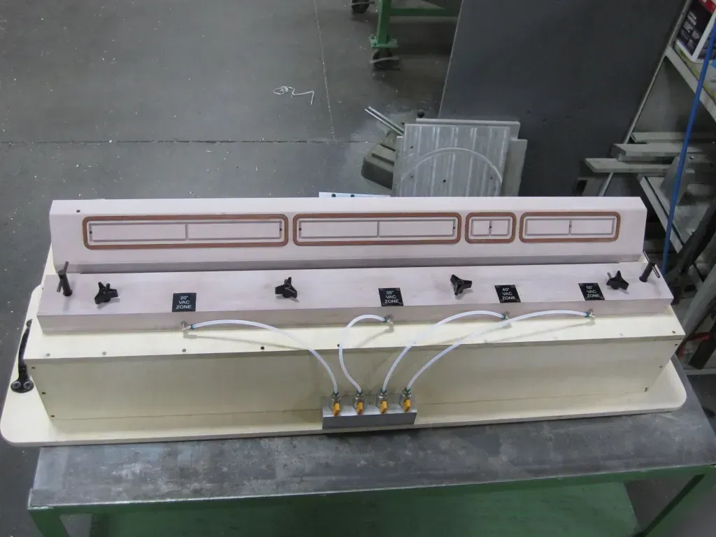 Long rectangular industrial machine with white base and wiring on a metal workbench in a workshop.