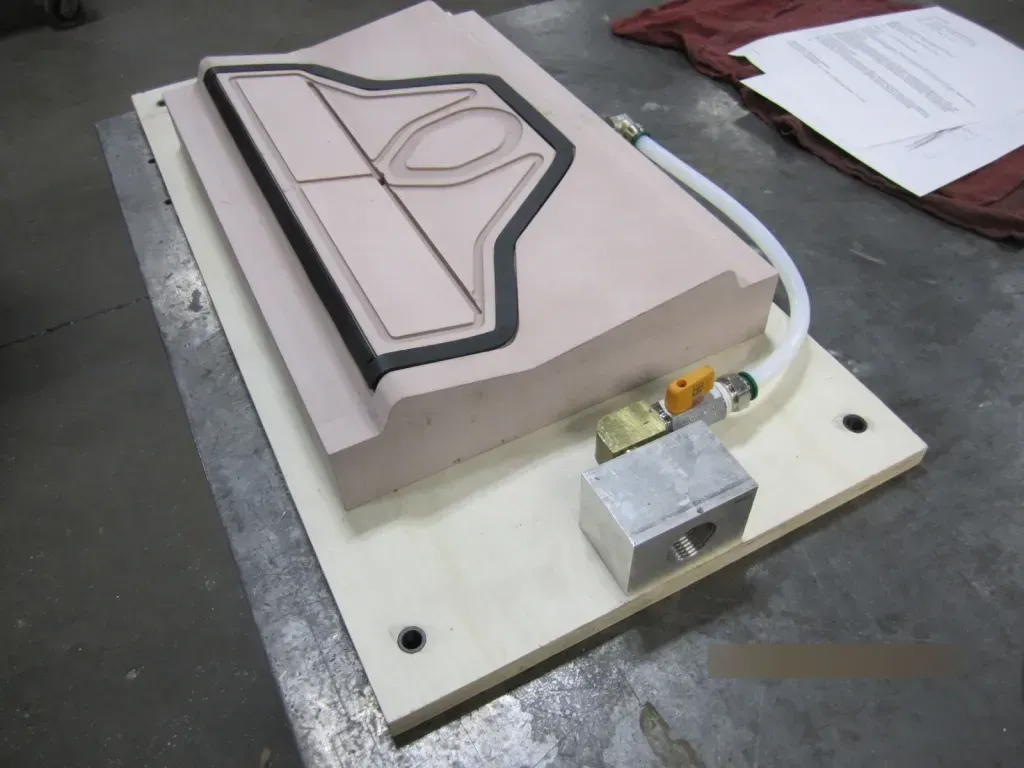 Prototype mold on a workbench, with a white base, gray block, and attached tubing in a workshop setting