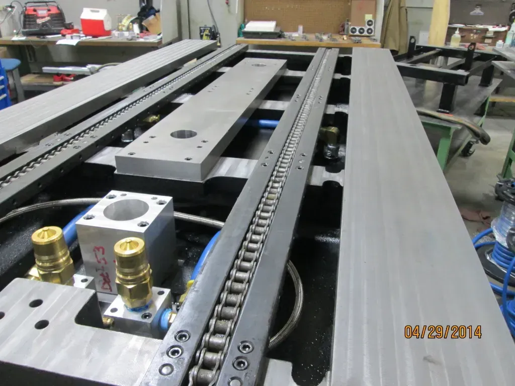 Industrial machine rails and chain drive assembly in a workshop with metal components and tools.