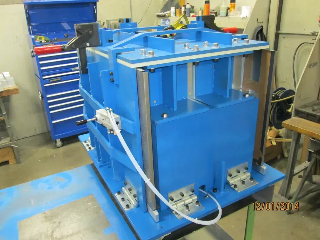 Blue industrial machine in a workshop beside a tool cabinet and workbench, with hoses attached