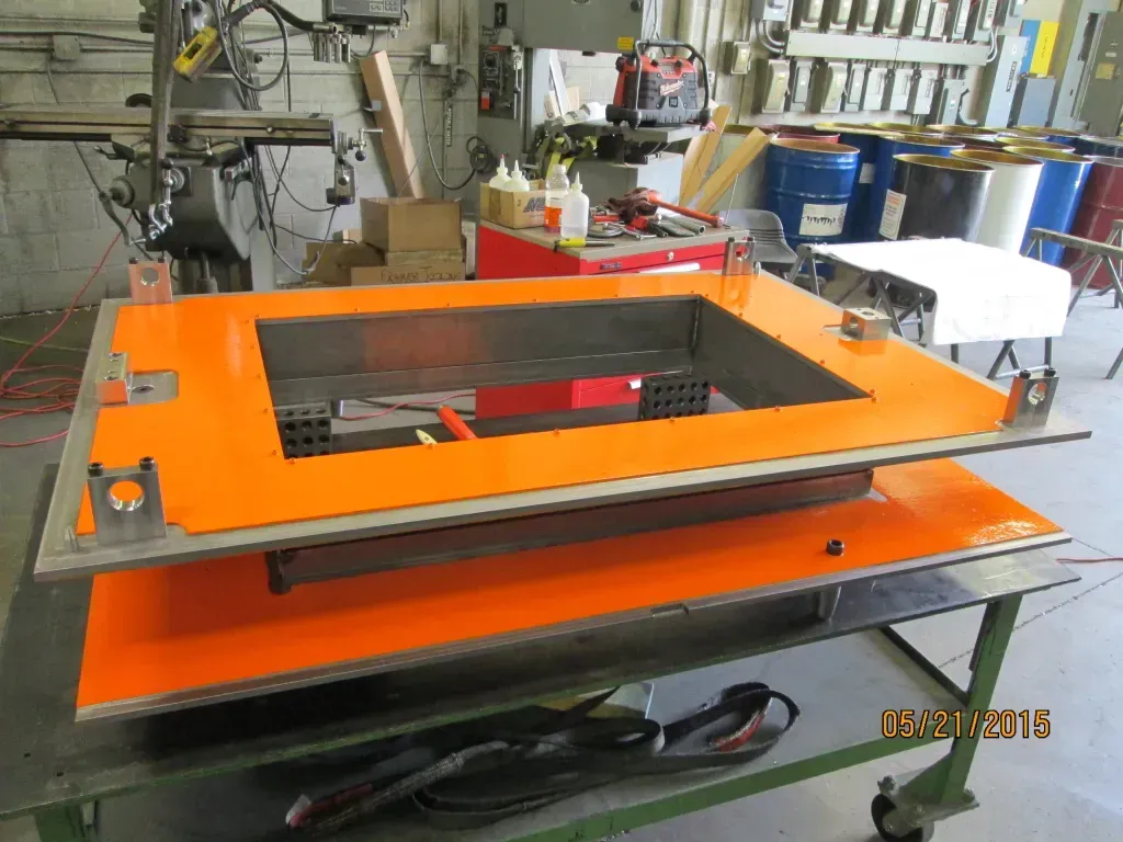Orange industrial machine frame with a black center opening in a workshop setting