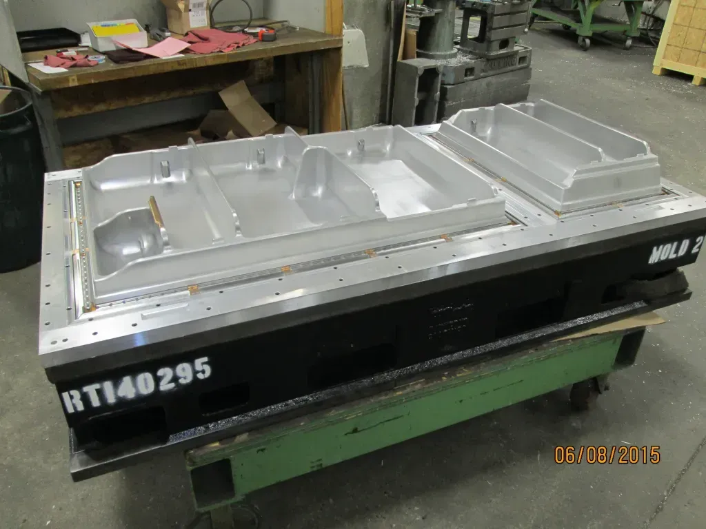 Silver metal machine part on a green cart in a workshop, with black panel labeled RT140295